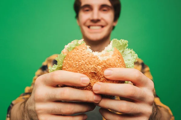 Close-up jongeman houdt hamburger met plezier, geïsoleerd op groene achtergrond — Stockfoto
