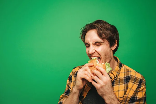 Jongeman eet hamburger met plezier, geïsoleerd op groene achtergrond — Stockfoto