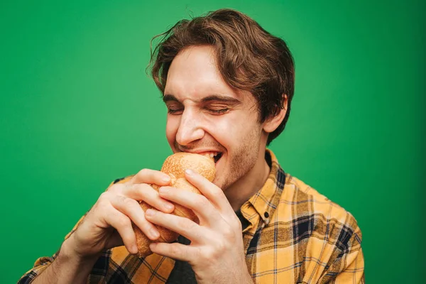 Young man bites croissant, isolated on green background