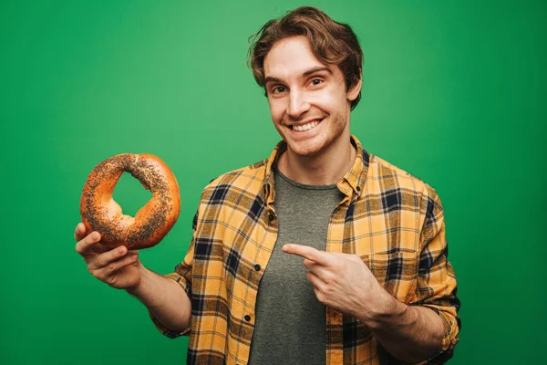 Jongeman houdt bagel, geïsoleerd op groene achtergrond — Stockfoto