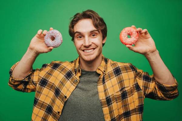 Mutlu adam donutları tutar, yeşil arka planda izole edilmiş. — Stok fotoğraf