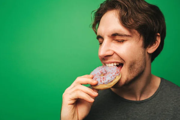 Jongeman bijt donut met plezier, geïsoleerd op groene achtergrond — Stockfoto