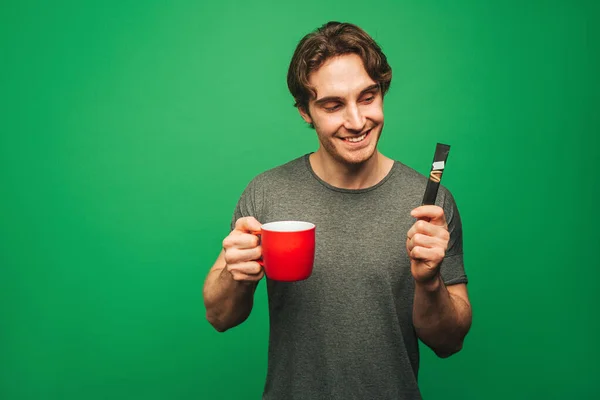 De mens is blij over het bereiden van een instant koffie, geïsoleerd op groene achtergrond — Stockfoto