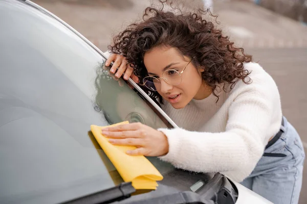 European girl cleaning car windshield with rag