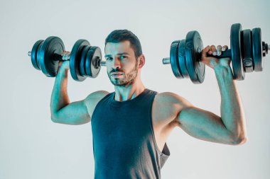 Genç adam dambılı omuz kaslarını çalıştırıyor.