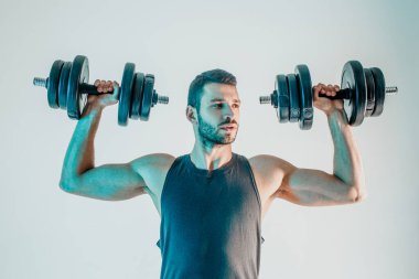 Genç adam dambılı omuz kaslarını çalıştırıyor.