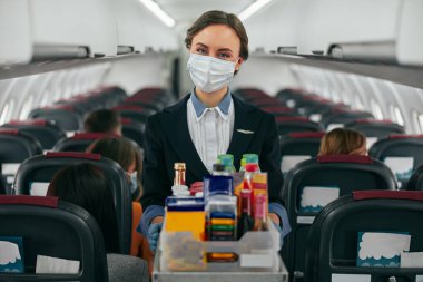 Hostes uçak kabininde yemek arabası taşıyor.