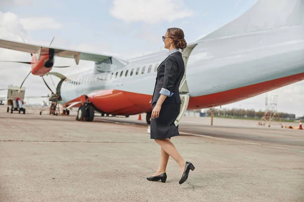 Стюардесса идет по взлетно-посадочной полосе возле самолета — стоковое фото