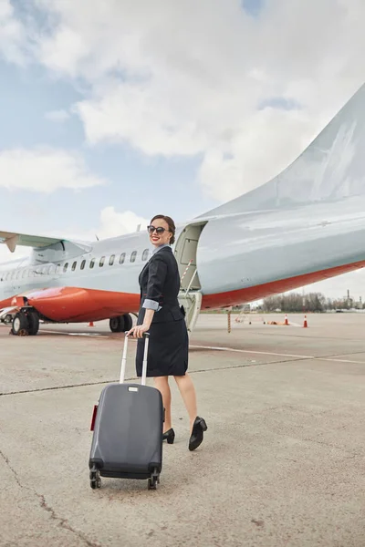 Azafata caminando con equipaje en pista cerca de avión — Foto de Stock