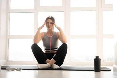 Başı ağrıyan sporcu kadın spor minderinde oturuyor.