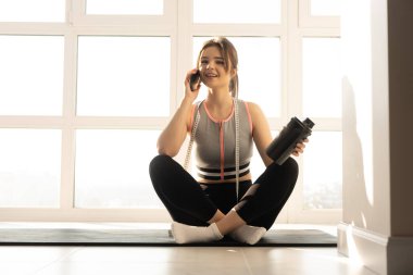 Sporcu kadın spor minderinde cep telefonuyla konuşuyor.