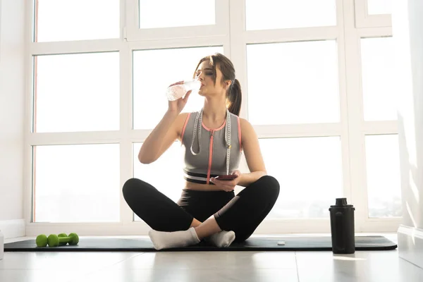 Mujer bebiendo agua de la botella en la colchoneta de fitness — Foto de Stock