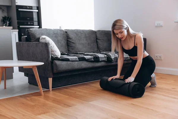 Mujer europea recogiendo alfombra de fitness en casa — Foto de Stock