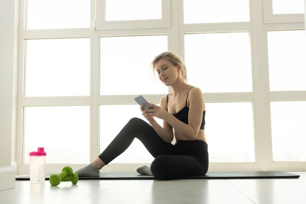在健身垫上使用手机的女运动员 — 图库照片