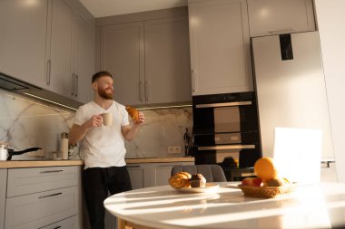 Adam kruvasan yiyor ve kahvaltıda çay içiyor.