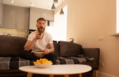 Şaşırmış bir adam kanepede oturup televizyon ya da film izler.