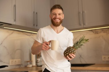 Adam fincandan çay içiyor ve ananas tutuyor.