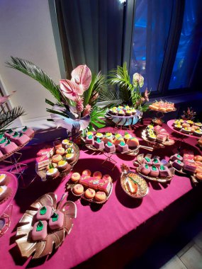 Kare piramidin etrafında değişik şekillerde pastalar olan tatlı bir masa. Kırmızı elbiseli bir masa.