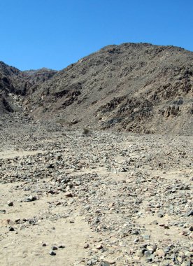 Mavi gökyüzü ile gri dağın yanındaki kayalık toprak