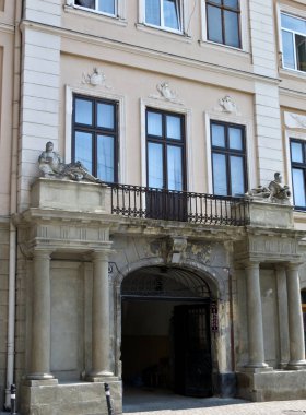 Eski binanın içinden geçen kemerli bir geçit. Sütunlarda taş heykeller ve balkonun demir çitleri var.