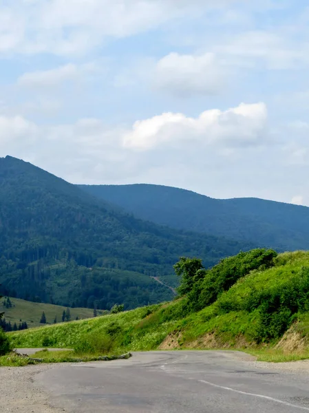 緑の森と茂みと雲と青空を背景に山のアスファルト道路 — ストック写真