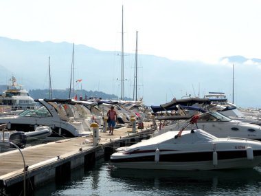 Budva / Montenegro - July 21, 2014: Pier with moored to it on the pier motor boats and sailing yachts in the town of Budva, Montenegro. Silhouettes of mountains in the di