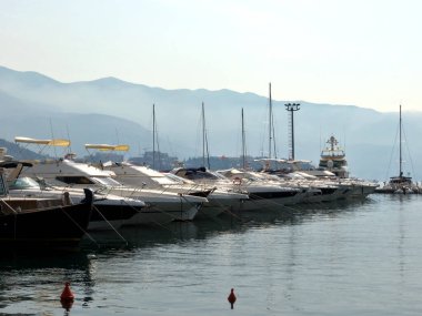 Budva Karadağ 'ın rıhtımındaki rıhtımda beyaz motorlar. Arka planda sisli dağların siluetleri
