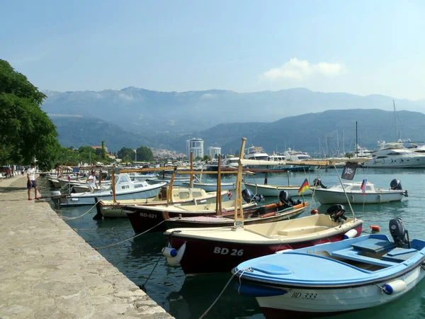 Budva / Montenegro - July 21, 2014: Fishing boats are moored on the water at the pier near the promenade of the city of Budva Montenegro. City and silhouettes of mountains in the background with clouds