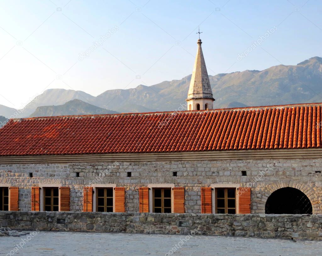 Old stone building with shuttered windows. Bell tower and mountains in the background
