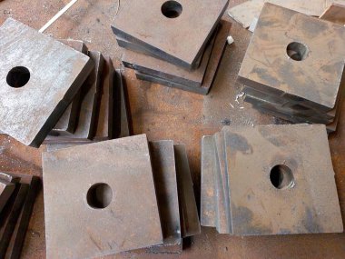 Metal kare parçalar bir atölyedeki tezgah üzerinde düzenlenir. Çeşitli bileşenleri güvenli bir şekilde bağlamak için tasarlanmışlardır..