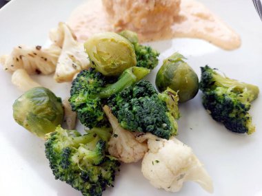 Tabakta brokoli, Brüksel lahanası ve karnabahar da dahil olmak üzere buharda pişirilmiş sebzelerin küçük bir porsiyon sos ve tahıl tabağının yanında yer alır..