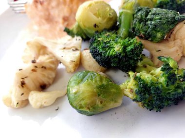 Brokoli ve Brüksel lahanası gibi buharda pişirilmiş sebzeler bir tabakta taze renklerini ve bir mutfakta yapılan yemek hazırlığı sırasında sağlıklı cazibelerini gösteriyorlar..