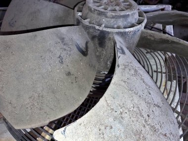 Pervane pervanesi toprak izleri gösterir ve atölyede yıpranır. Bıçaklar metal bir kafesin üzerinde, çeşitli aletler ve ekipmanlarla çevrili..