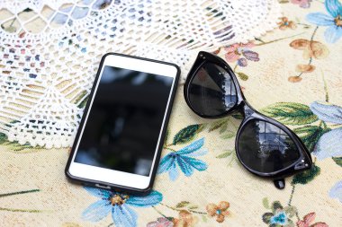 Şablon. Çiçekli masa örtüsü üzerinde telefon. Dantel peçete ve gözlük