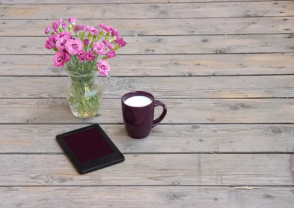 Die Tablette, eine Blumenvase und eine Tasse Kaffee mit Milch Stockbild