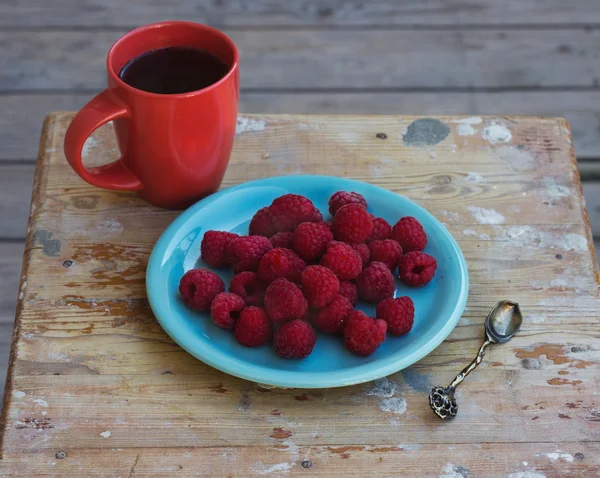 Frambozen op een plaat met een kopje koffie op het terras — Stockfoto