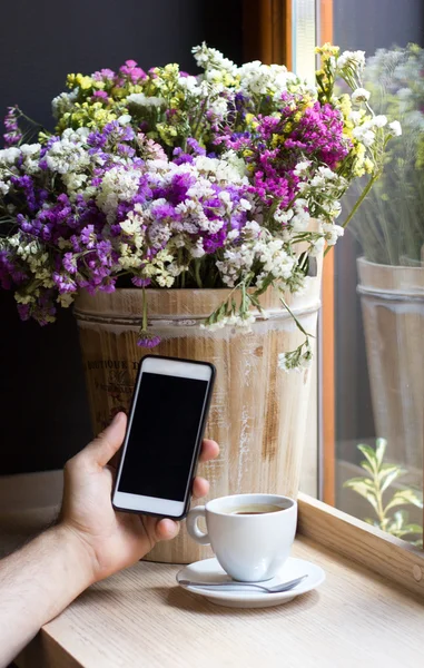 Phone in the hand with flowers. template. At the window on a wooden table.