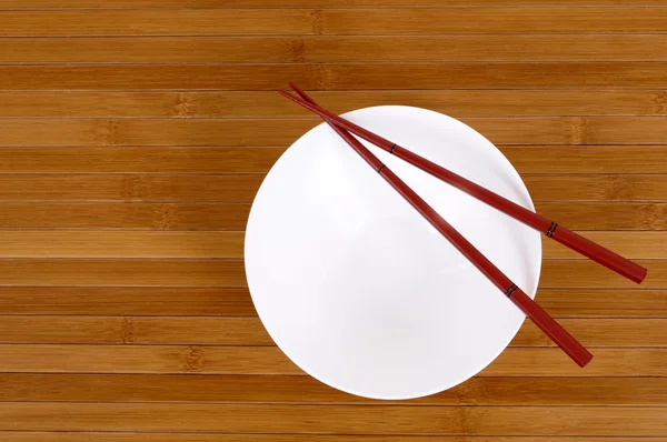 White empty rice bowl with wooden chopsticks on a bamboo background — Stock Photo, Image