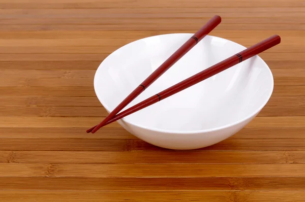 Белая пустая рисовая миска с деревянными палочками на бамбуковом фоне — стоковое фото