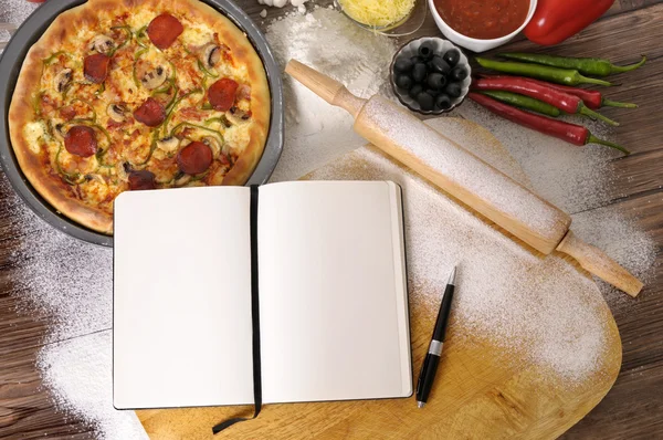 Pizza met notebook en ingrediënten — Stockfoto