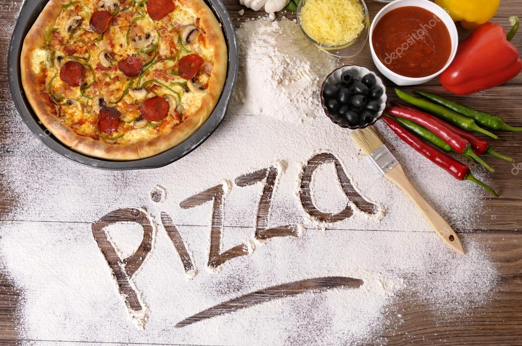 The word Pizza written in flour with various ingredients.