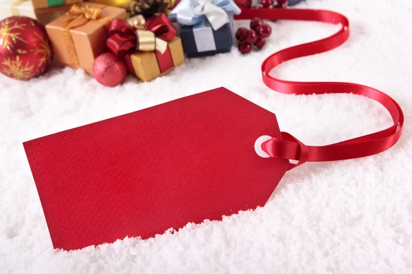 Etiqueta de presente vermelho que coloca em um fundo de neve — Fotografia de Stock
