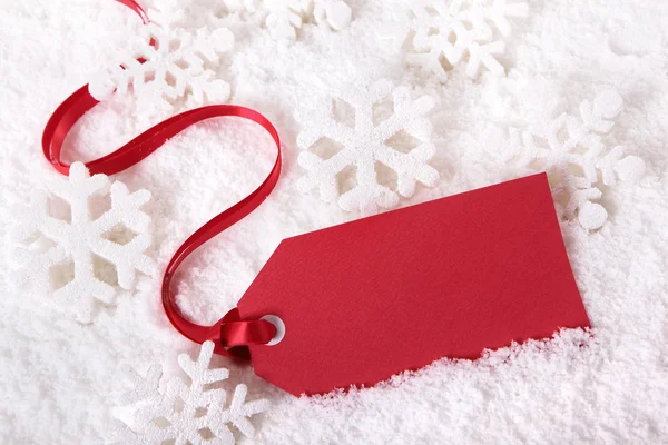 Etiqueta de regalo roja que pone en la nieve con copos de nieve, espacio de copia —  Fotos de Stock