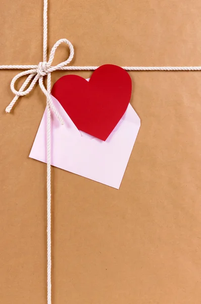 Regalo de San Valentín con tarjeta de corazón rojo o etiqueta de regalo, paquete de papel marrón — Foto de Stock