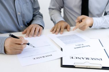 İki işadamı masaya oturup sigorta belgelerini imzalarlar.