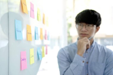 Bardaktaki poz kağıdını izleyen bir işadamı, bir iş planına ilham vermek için birçok anahtar kelime yazıldı..