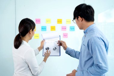 İş adamları ve kadınlar ayakta duruyor. Bir ideal bulup not almak ve tahtaya yapıştırmak için tavsiye ve beyin fırtınası yapıyor..