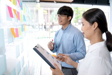 İş adamları ve kadınlar ayakta duruyor. Bir ideal bulup not almak ve tahtaya yapıştırmak için tavsiye ve beyin fırtınası yapıyor..