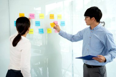 İş adamları ve kadınlar ayakta duruyor. Bir ideal bulup not almak ve tahtaya yapıştırmak için tavsiye ve beyin fırtınası yapıyor..