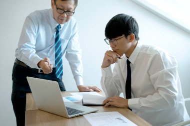 Bir iş adamı danışmanı ve stajyer personel, iş eğitiminde koçluk yaparken elinde kitap notuyla danışman olarak otururlar.